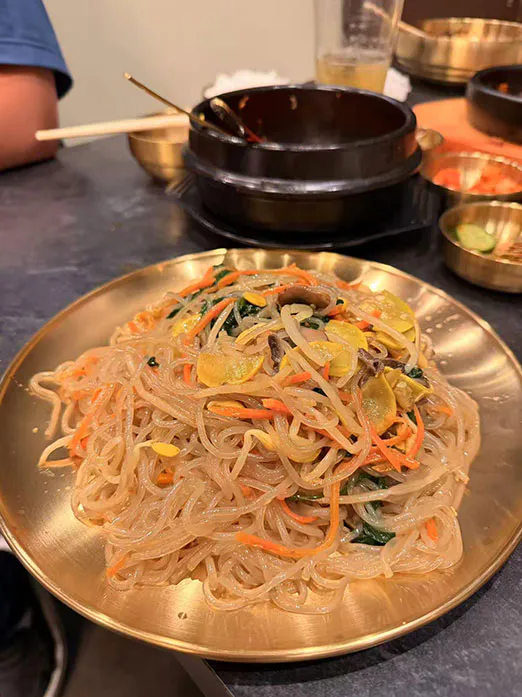 Stir-fried glass noodles with vegetables on a golden plate at Mr.Kimchi Korean Bistro, a Korean Restaurant in Oklahoma City